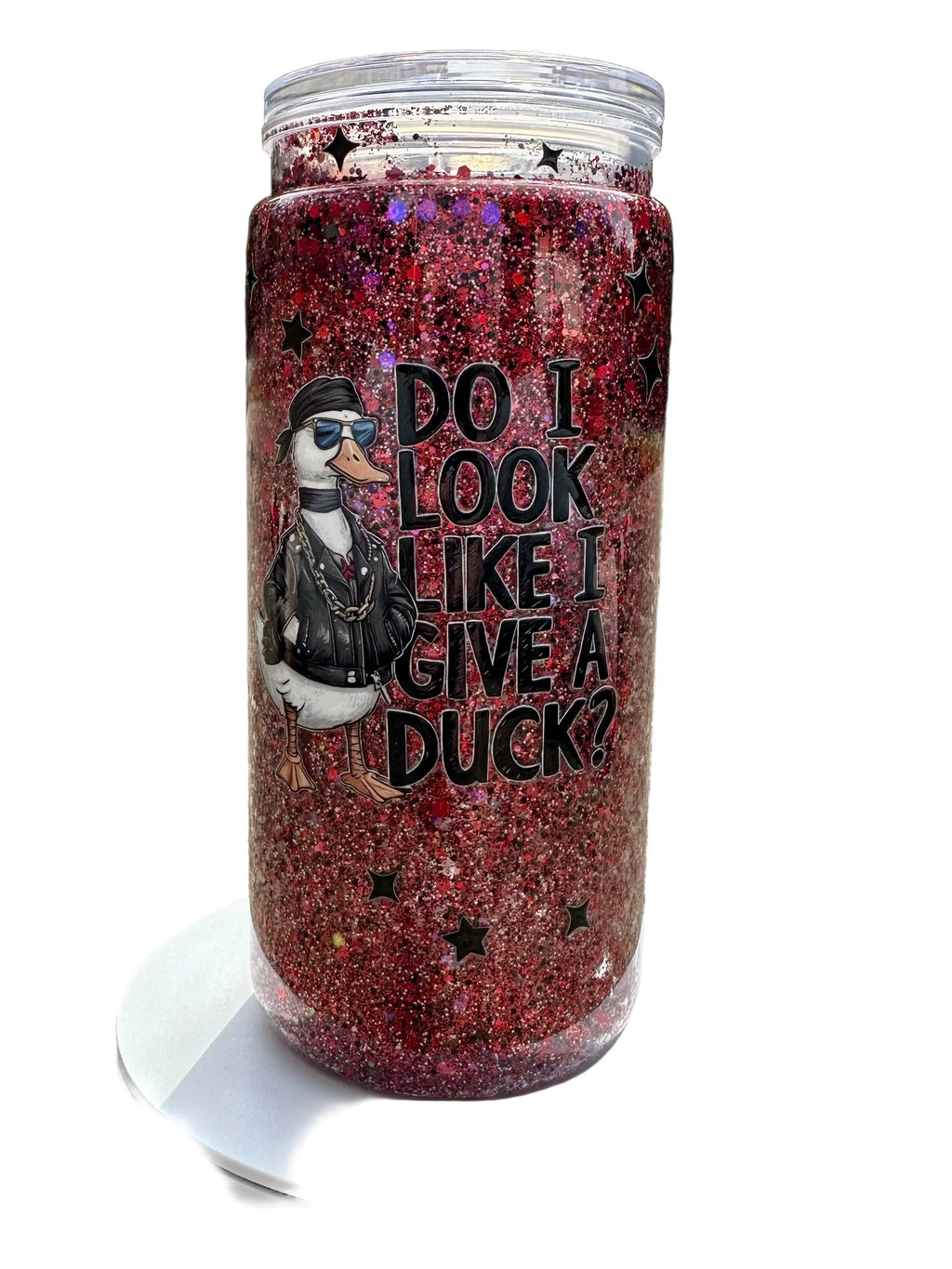 Tumbler with glittery red design and text 'Do I look like I give a duck?' on a white stand outdoors.